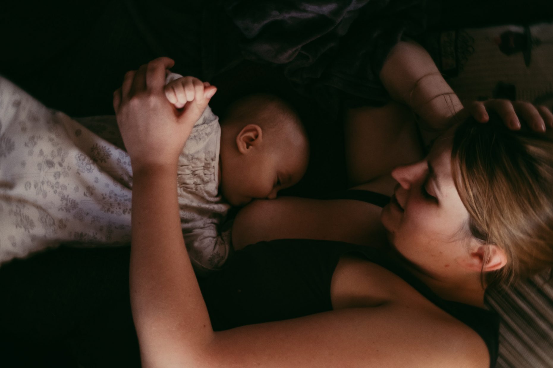Mutter liegt auf dem Bett und stillt ihr Baby. Stillfoto roar Familienfotograf Köln und Düsseldorf