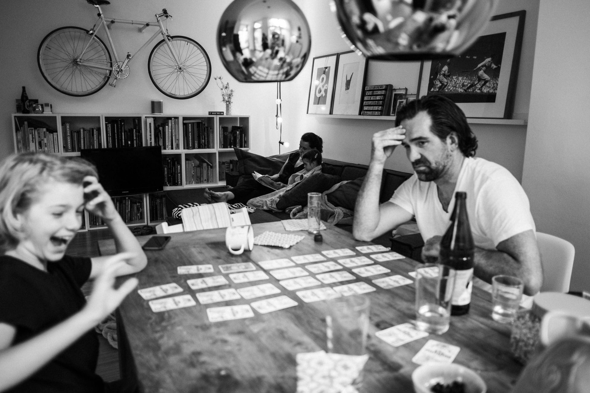 Vater und Sohn spielen ein Brettspiel m Vordergrund und im Hintergrund schauen Mama und Tochter ein Buch an