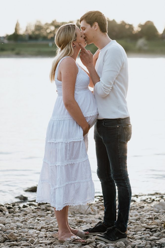 Küssendes Pärchen während eines Babybauchshootings im Gegenlicht