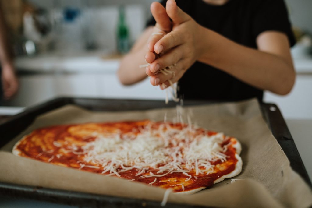 Junge streut Käse auf Pizza